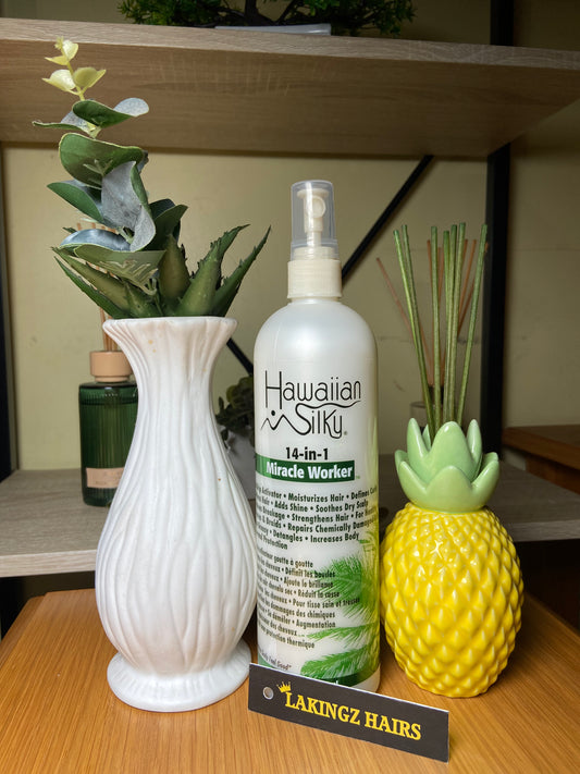 A bottle of Hawaiian Silk 14-in-1 Miracle Worker hair care spray displayed on a wooden shelf alongside decorative props. 'LAKINGZ HAIRS'